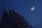 Waning moon over Thai temple roof at night