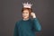 Wannabe king. Close up of ginger young good-looking male teenager in stylish green sweater folding paper crown on stick