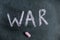 War. A word is written in pink chalk on a black chalkboard. Handwritten text. A piece of colored chalk hangs next to it