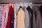 A wardrobe with clothes,summer children`s dresses and autumn and winter clothes for adults hang on a shelf in the closet