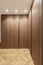 Wardrobe with root wood doors with full-length handles in the room with herringbone oak flooring, false ceiling spotlights and