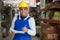 Warehouse male worker in protective helmet and overalls counts the quantity of goods and writes in notebook