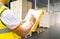 Warehouse worker holding clipboard writing on paper checklist for delivering shipment boxes on pallets.