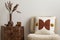 Warm and cozy interior with boucle armchair, stylish patterned pillow, wooden coffee table, vase with dried flowers and personal