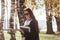 Warm days. Young smiling brunette in sunglasses stands in the park near the trees and holds notepad