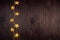 Warm elegant lights garland with golden stars on dark brown wood board, top view, copy space, New Year background.