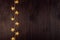 Warm elegant lights garland with golden stars on dark brown wood board, top view, copy space, New Year background.