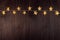 Warm elegant lights garland with golden stars on dark brown wood board, top view, copy space, New Year background, horizontal.