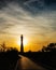 Warm golden hour light illuminates the pathway to the silhouette of a lighthouse during sunset. Fire Island NY