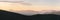 Warm gradient of dawn sky above layers of mountain and rock silhouettes. Vivid alpine landscape with dark rockies and orange