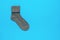 Warm grey knitted sock on a light blue background. Minimal footwear concept