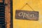 A warm, inviting rustic wooden 'Open' sign adorns a vibrant yellow stucco wall.