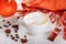 Warm knit scarf and cup of hot coffee with foam. Halloween orange pumpkin, spices and other holiday decor. Side view