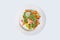 Warm salad of red fish and slices of French fries with vegetables on a white plate. An isolated object.Top view