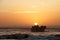 Warm toned image of a sunset with a ship wreck and a flock of sea birds silhouetted against the sunset