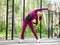 Warming up before workout. Fit caucasian young woman in magenta sportswear does side bends in sports area outdoor in