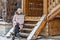 Warmly dressed young woman posing on the porch of a wooden house in the village. Winter holidays in the countryside