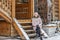 Warmly dressed young woman posing on the porch of a wooden house in the village. Winter holidays in the countryside