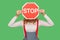 Warning of ban, no access. Portrait of anonymous woman in stylish overalls covering face with octagonal red Stop traffic sign