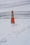 Warning orange cone on icy road turn. Car tire traces on the snowy road.