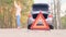 Warning red triangle. Gray car with flashing emergency light along the road after an accident. The trunk is open. A