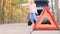 Warning red triangle. Sad young woman sits in trunk of gray car with flashing emergency light along road waiting for