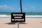 Warning sign on beach next to the trunk of a palm tree on a sunny day with a blue clear sky warning that it is hurricane season