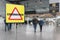 Warning sign with text Coronavirus on a generic airport with passengers walking towards the boarding gates