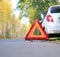 Warning stop sign on the road against the background of a white car and forest. concept of roadside assistance, travel incidents,