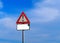 Warning triangular sign with exclamation mark. A worn white signpost is below, without text.