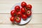 Washed red ripened cherry tomatoes on white plate on light wooden table