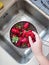 Washed ripe juicy red strawberries in mesh strainer above sink