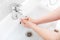 Washing femle hands in a ceramic washbasin with a chrome-plated faucet.