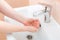 Washing femle hands in a ceramic washbasin with a chrome-plated faucet.