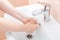 Washing femle hands in white ceramic washbasin with a chrome faucet.