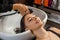 Washing procedure. Beautiful young woman with hairdresser washing head at hair salon