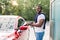 Washing of red modern car on open air self car wash service with foam and high powered hose. Young smiling African man