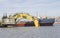 The water area of the port. A floating excavator with a yellow dipped boom next to the barge