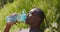 Water balance concept. Young thirsty african american guy drinking fresh water from plastic bottle, lying on grass