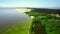 Water bay and green shoreline with little village on it are filmed by drone on a summer day