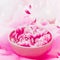 Water bowl with pink flowers and flying petals standing at pink silk. Close up. Beauty and spa concept