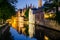 Water canal, medieval houses and bell tower at night in Bruges