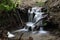 Water cascade in the creek. Motion photography. Slow shutter speed. Focus on waterfall, blurred leaves