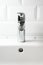 Water dripping from the tap into white ceramic sink and white tile wall, vertical