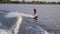 Water extreme sport, wakeboarder man holds rope handle and rides on board on river in slow motion with splashes on