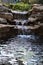 Water falls at the end of the pond lined by rocks and plants