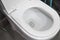 Water flushing in toilet bowl. White hanging toilet seat on white toilet in the home bathroom with grey tiles in