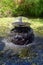 Water fountain with water cascading into a pretty peaceful pond with small tropical water lilies in dappled sunlight.