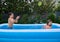 Water fun day in a backyard. Happy children playing and splashing each other with water in the inflatable swimming pool