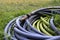 Water hose with metal nozzle coiled on green grass in garden